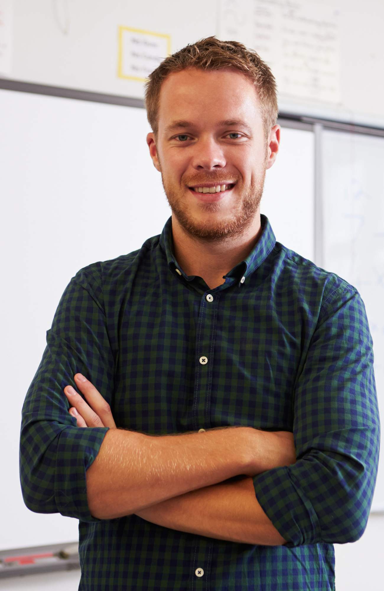 Person standing in front of a whiteboard with arms folded and smiling.