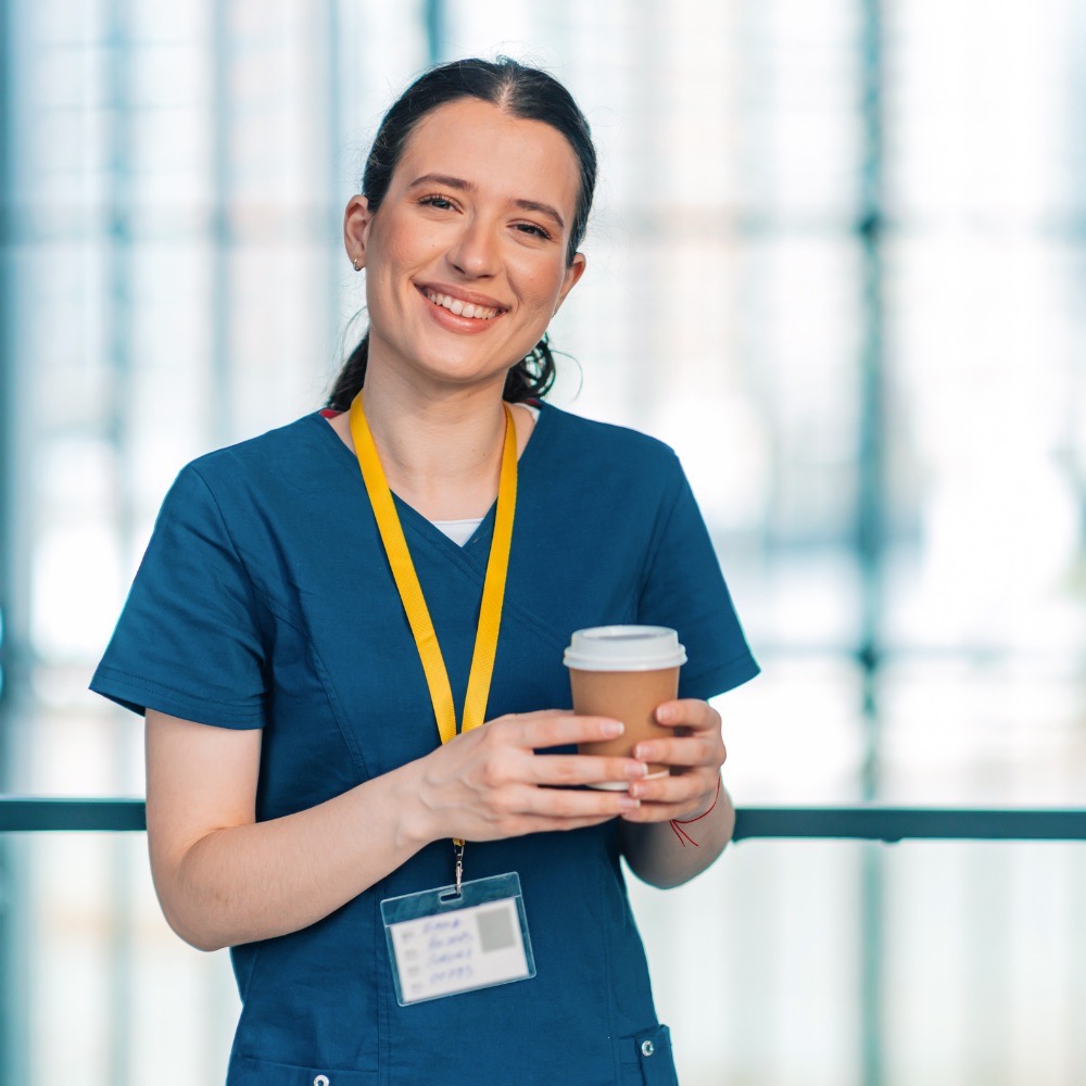 Person in health care uniform holding a coffee and smiling