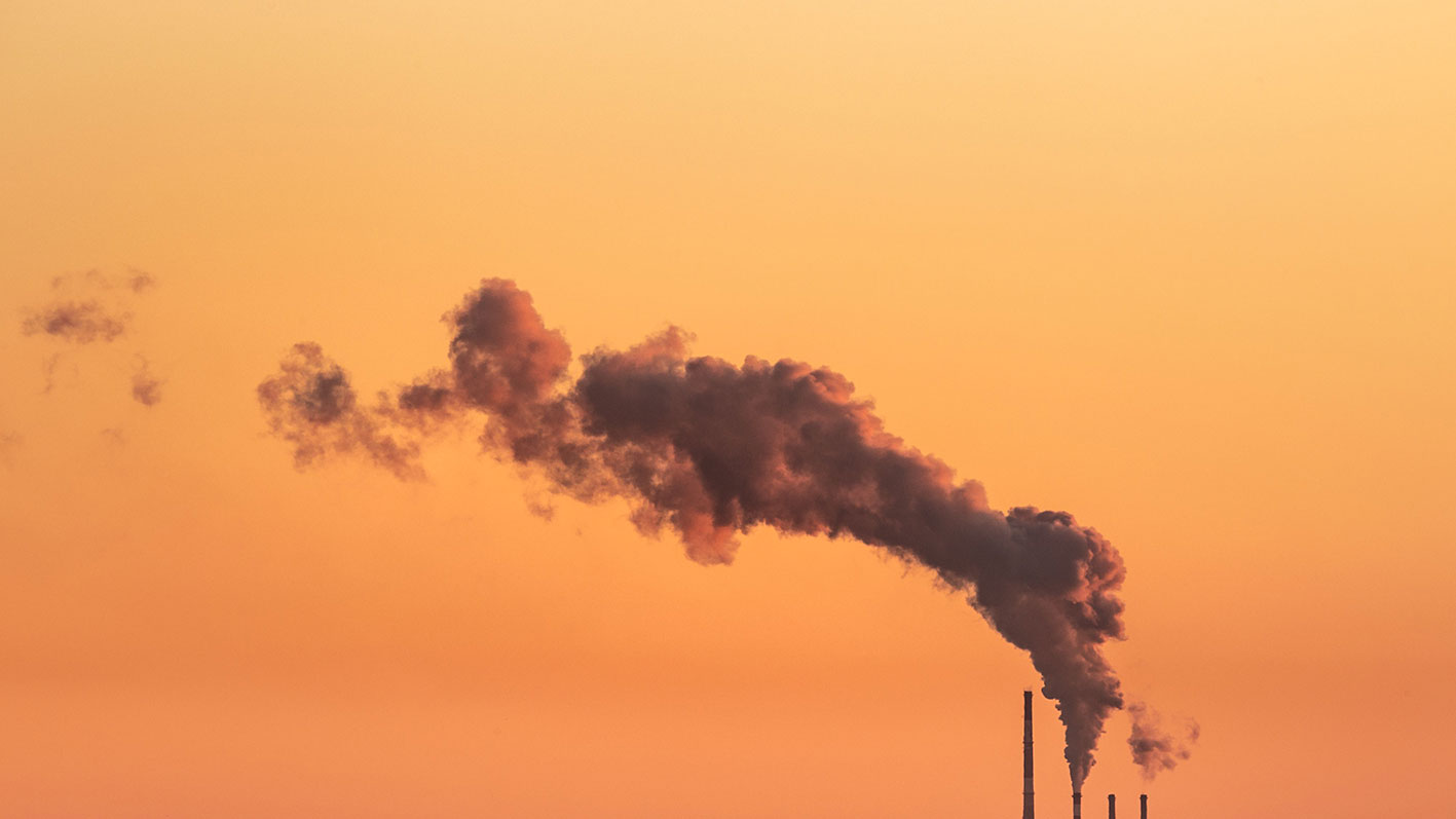 Industrial smokestacks emitting emissions at sunset, representing HVAC decarbonisation, carbon reduction strategies and feasibility studies for low-carbon building systems with Hysopt Feasibility.