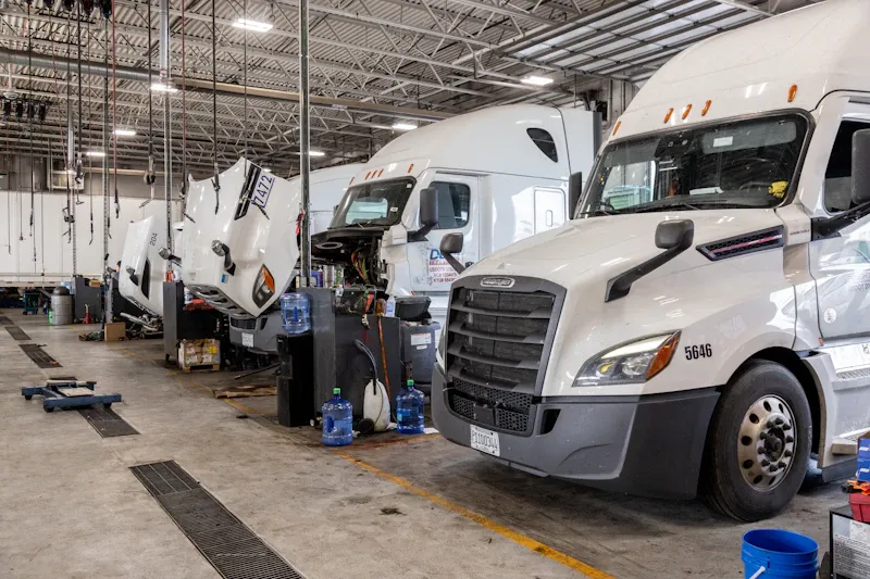 Heavy-duty truck repair shop with multiple semi trucks in service bays, including open hoods for maintenance and repairs.