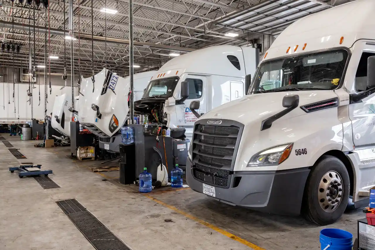 Heavy-duty truck repair shop with multiple semi trucks in service bays, including open hoods for maintenance and repairs.