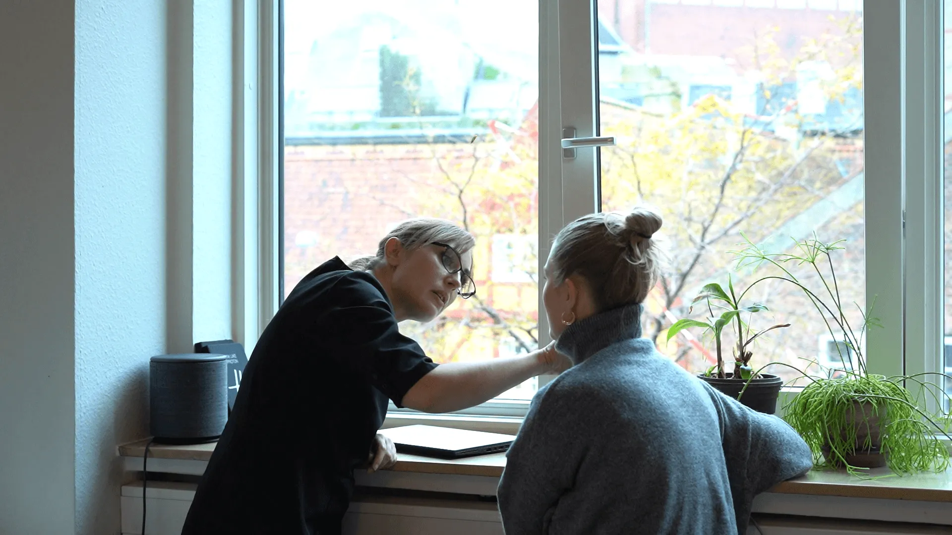 A woman is helping another woman put her hand on a window sill.