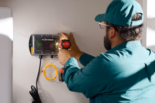 Water pooling on tiled bathroom floor around the base of a white toilet, indicating a leak.