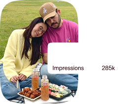 A man and woman are sitting on a blanket with food and drinks.
