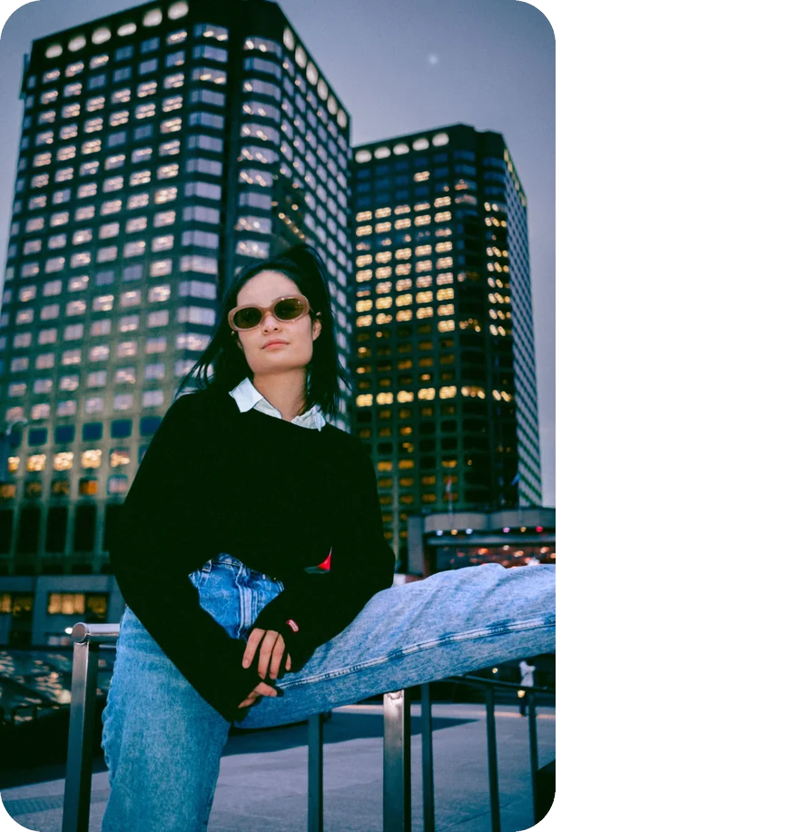 Creator in sunglasses leaning on a railing at dusk in front of downtown Montreal office towers