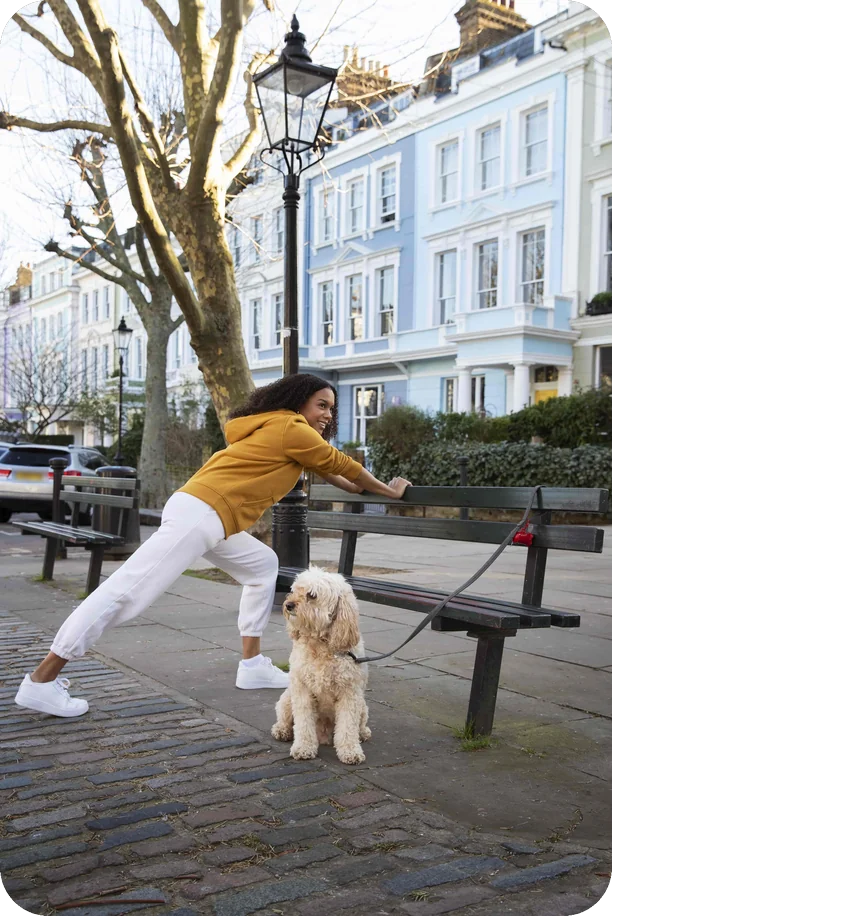 Woman stretching by a bench with her dog on a pastel terraced street in London