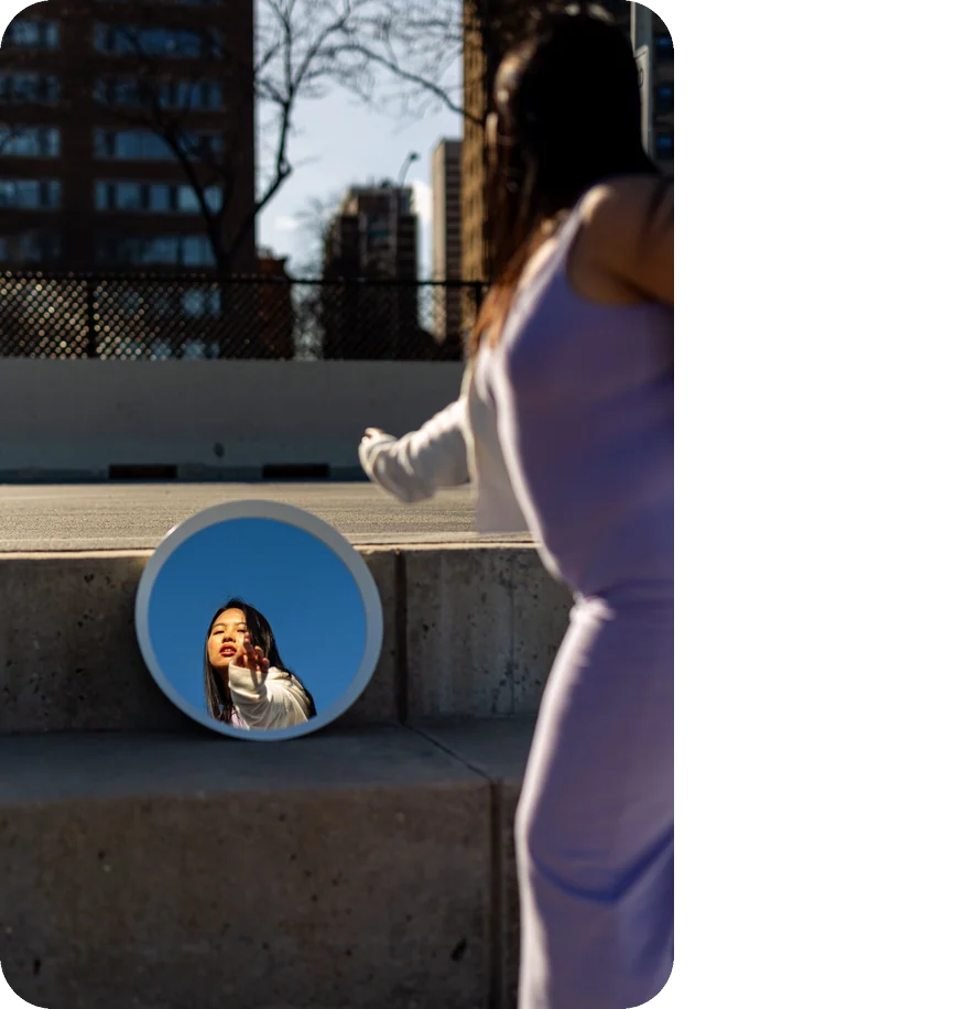 Creator reaching toward a mirror reflecting her against blue sky in downtown Chicago