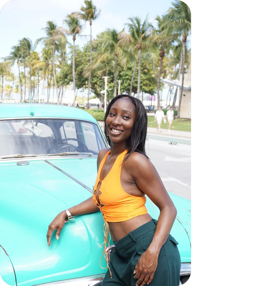 Woman smiling beside a turquoise vintage car on Ocean Drive in Miami Beach