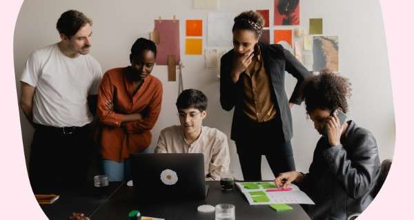 A man working on a laptop with a group of people standing around him.