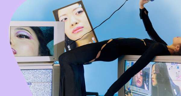 A woman wearing black leggings and a black dress is posing in front of a TV.