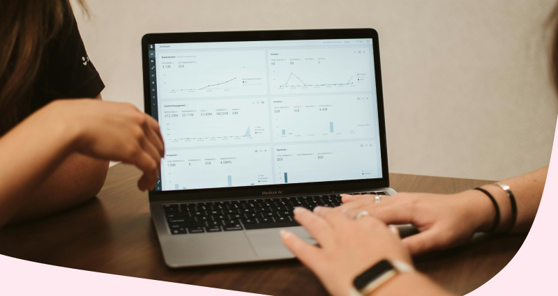 A person is typing on a laptop with graphs on the screen.