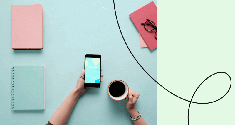 A person holding a cell phone and a cup of coffee.