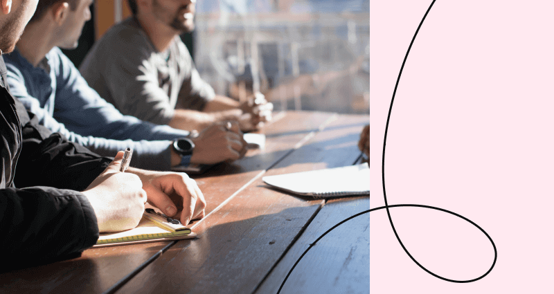 A man is writing on a notebook while sitting at a table.