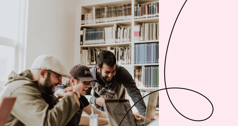 Three men sitting in front of a laptop, one of them is smiling.