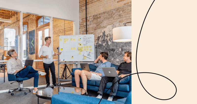 A man is sitting on a blue couch in front of a white board with sticky notes on it.