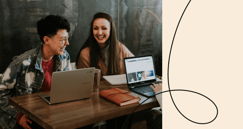 Two women sitting at a table with a laptop and a book.