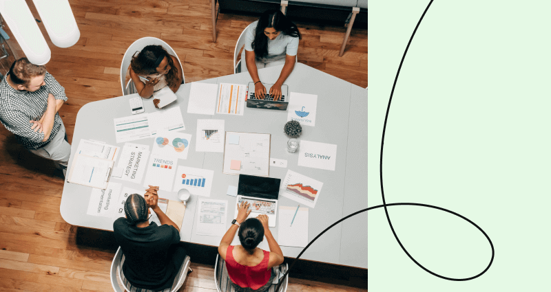 A group of people sitting around a table with a laptop and papers.