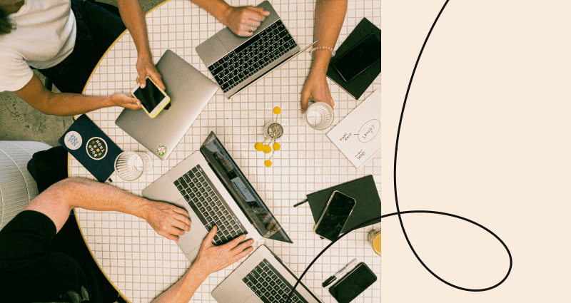 A group of people sitting around a table with laptops and cell phones.