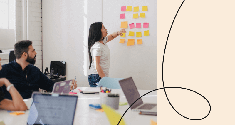A woman is standing in front of a white board with sticky notes on it.
