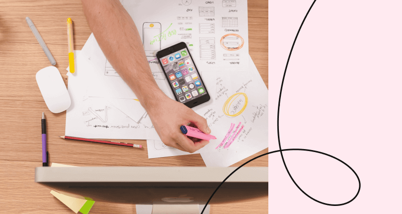 A man writing on a piece of paper with a cell phone on the desk.