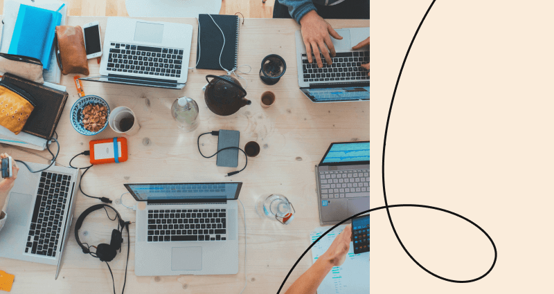 A person is typing on a laptop in front of a table with other laptops and a cup.