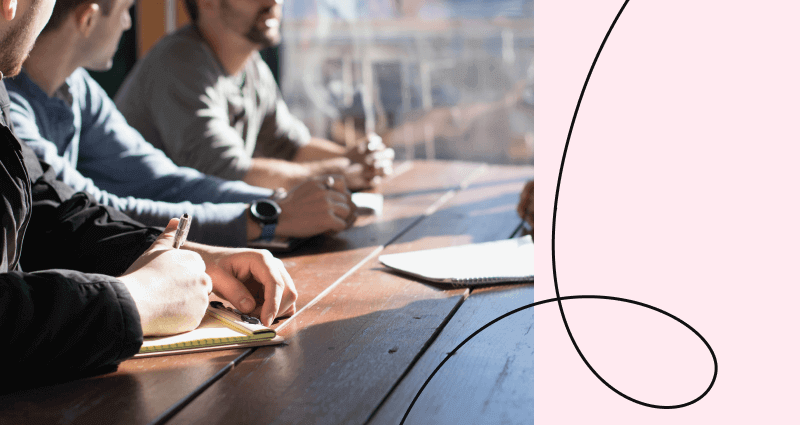 A man is writing on a notebook while sitting at a table.
