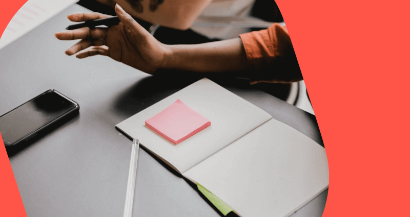 A person holding a book with a pink sticky note on the page.