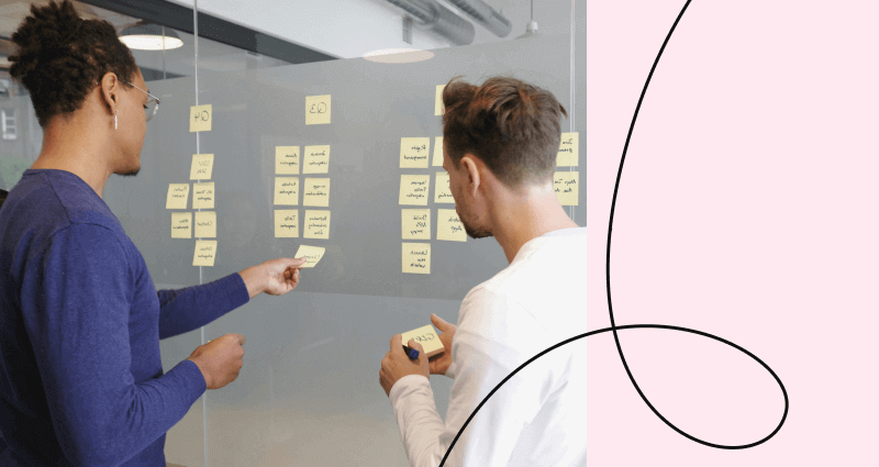 Two men are writing on a white board.