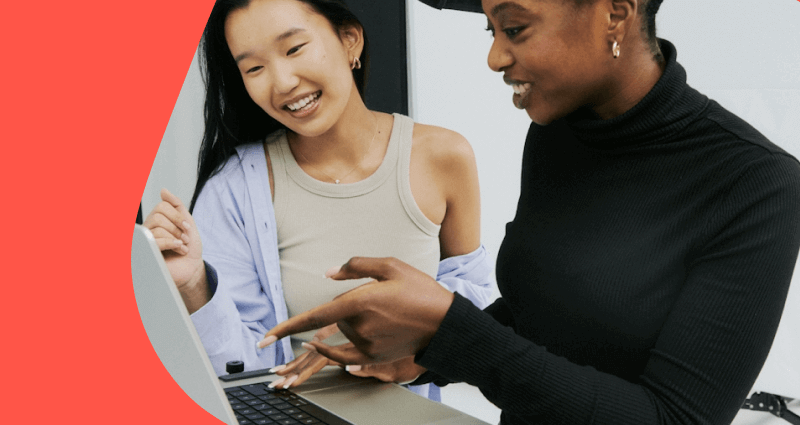 Two women are smiling and pointing at a laptop screen.