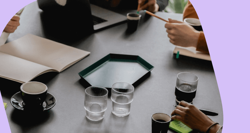 A group of people sitting around a table with cups and a notebook.