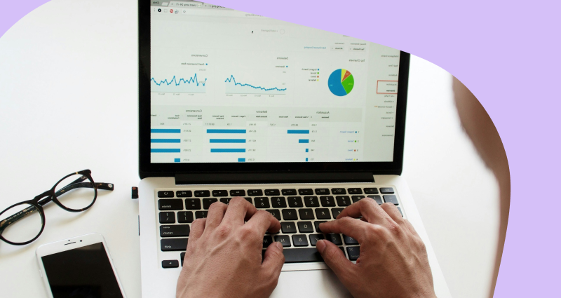 A person is typing on a laptop with graphs and charts on the screen.