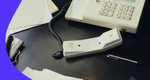 A white telephone with a black cord on a desk.