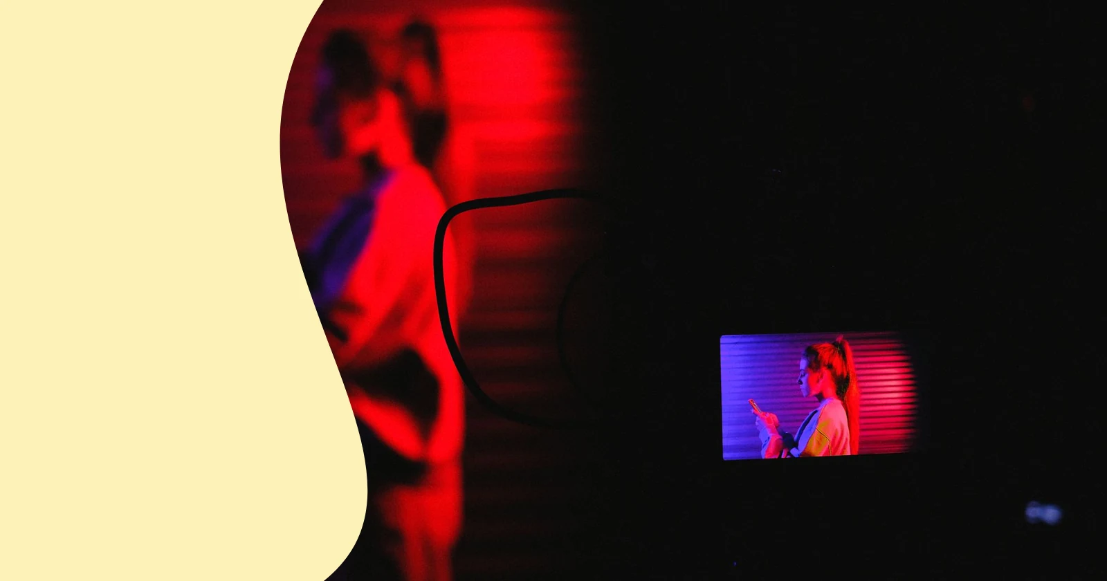 Side view of anonymous female standing and using smartphone while recording video on professional camera in dark room with neon lights