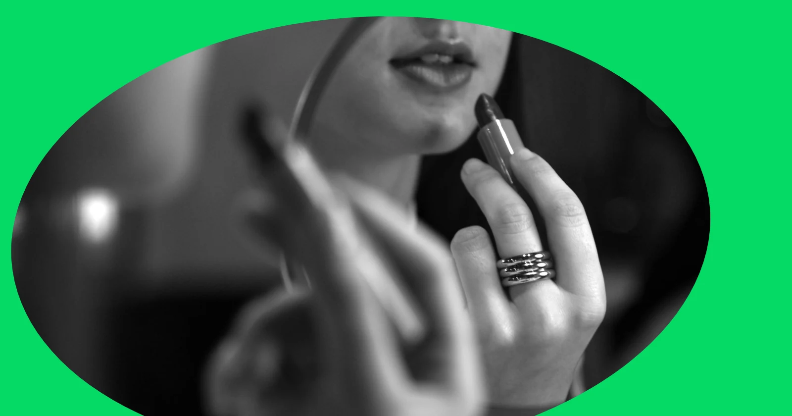 A woman applies lipstick in front of a mirror, wearing rings. Black and white style.