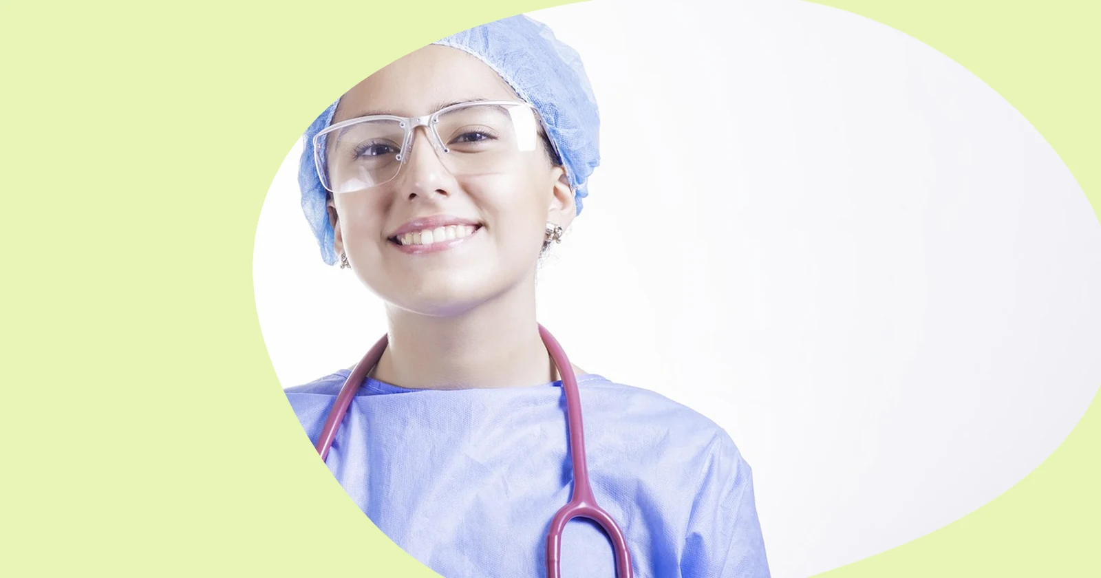 Smiling healthcare worker in blue scrubs, a surgical cap and safety glasses with a stethoscope around the neck.