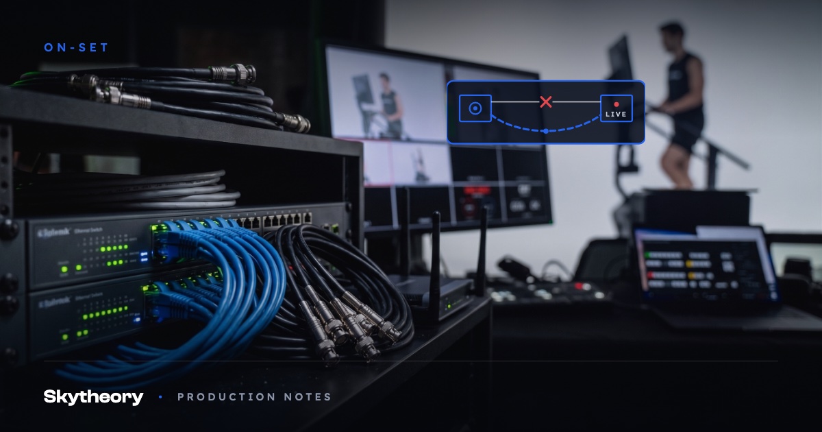 Broadcast network rack with ethernet switches, blue cabling, BNC coax and a bonded router with antennas, live multiview and talent on the studio cyc behind