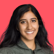 Smiling woman with long black hair wearing a green jacket against a bright pink background.