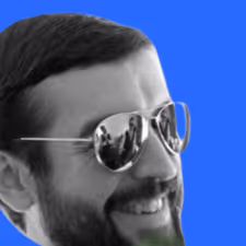 Close-up of a smiling man with a beard wearing reflective aviator sunglasses against a blue background.