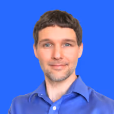 Portrait of a man with short brown hair and blue eyes wearing a blue collared shirt against a blue background.