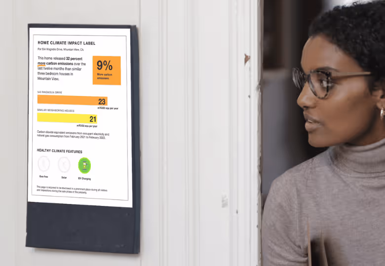 Woman with glasses looking at a home climate impact label on a door showing carbon emissions and healthy climate features.