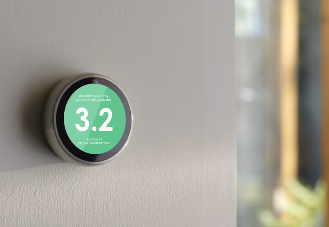 Round digital energy monitor on a wall showing California's electricity grid producing 3.2 kilotons of carbon dioxide per hour.