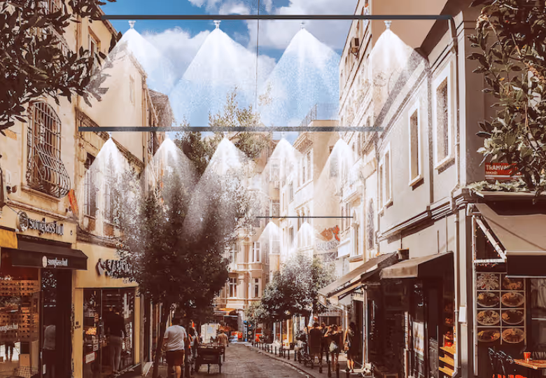 Outdoor misting system installed above a narrow pedestrian street with buildings and trees on both sides.