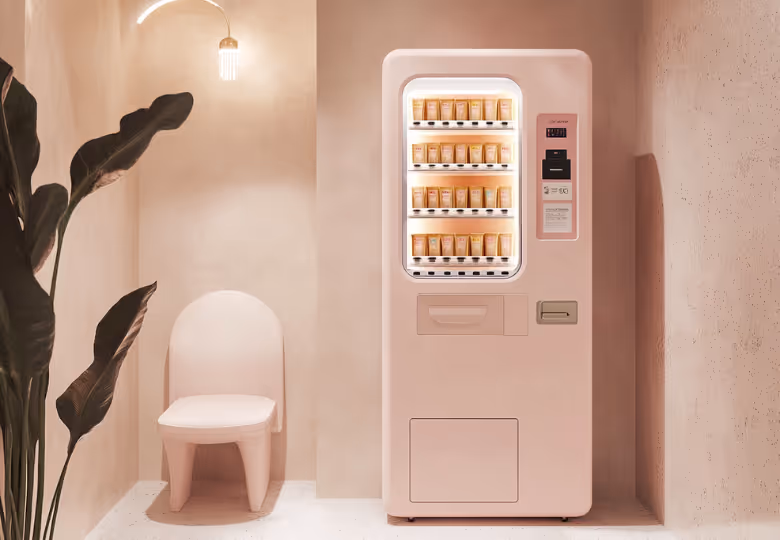 Minimalist room with a white chair, large green plant, and a vending machine stocked with skincare products.