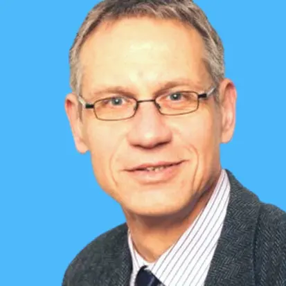 Middle-aged man with glasses, short gray hair, wearing a dark blazer, striped shirt, and dark tie against a blue background.