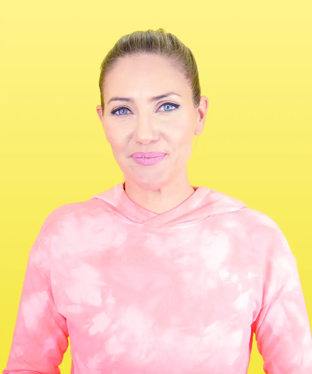 Woman with blue eyes and pink lipstick wearing a pink tie-dye hoodie against a yellow background.