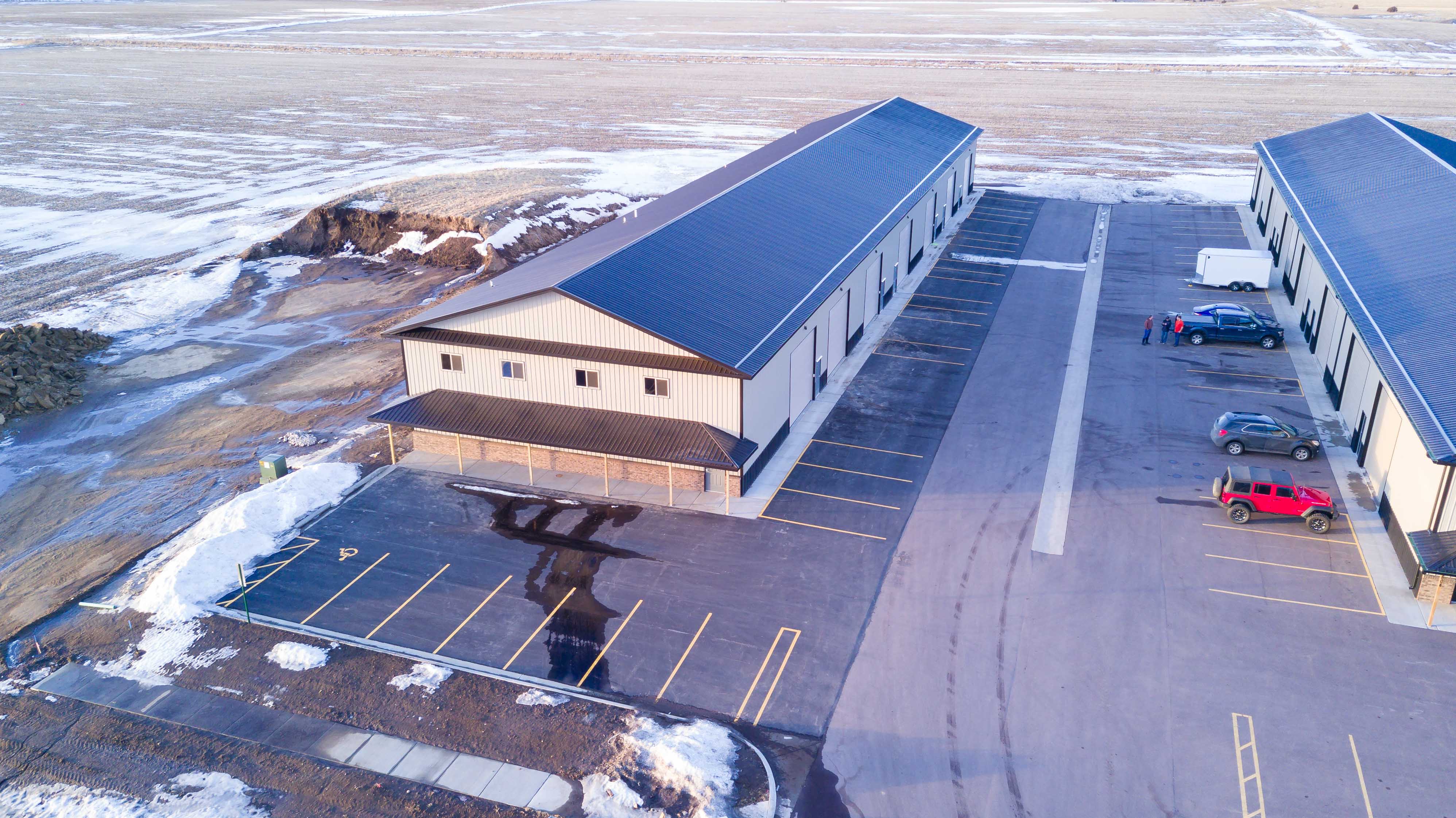 Aerial view of a new tan shop condo building with a covered front porch, striped parking and a snowy field behind