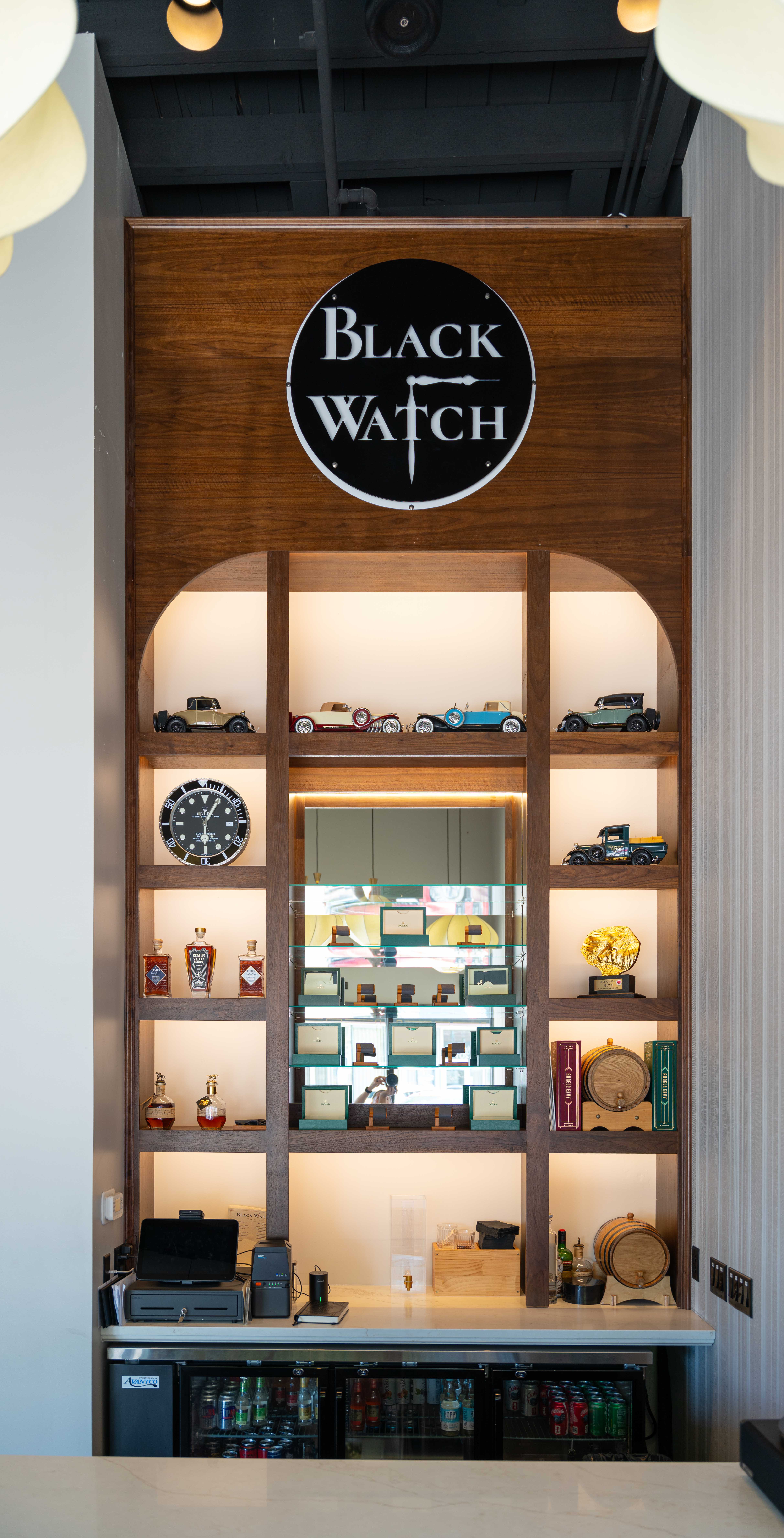 Tall arched walnut display shelving with model cars, a clock and a round Black Watch sign above the bar counter