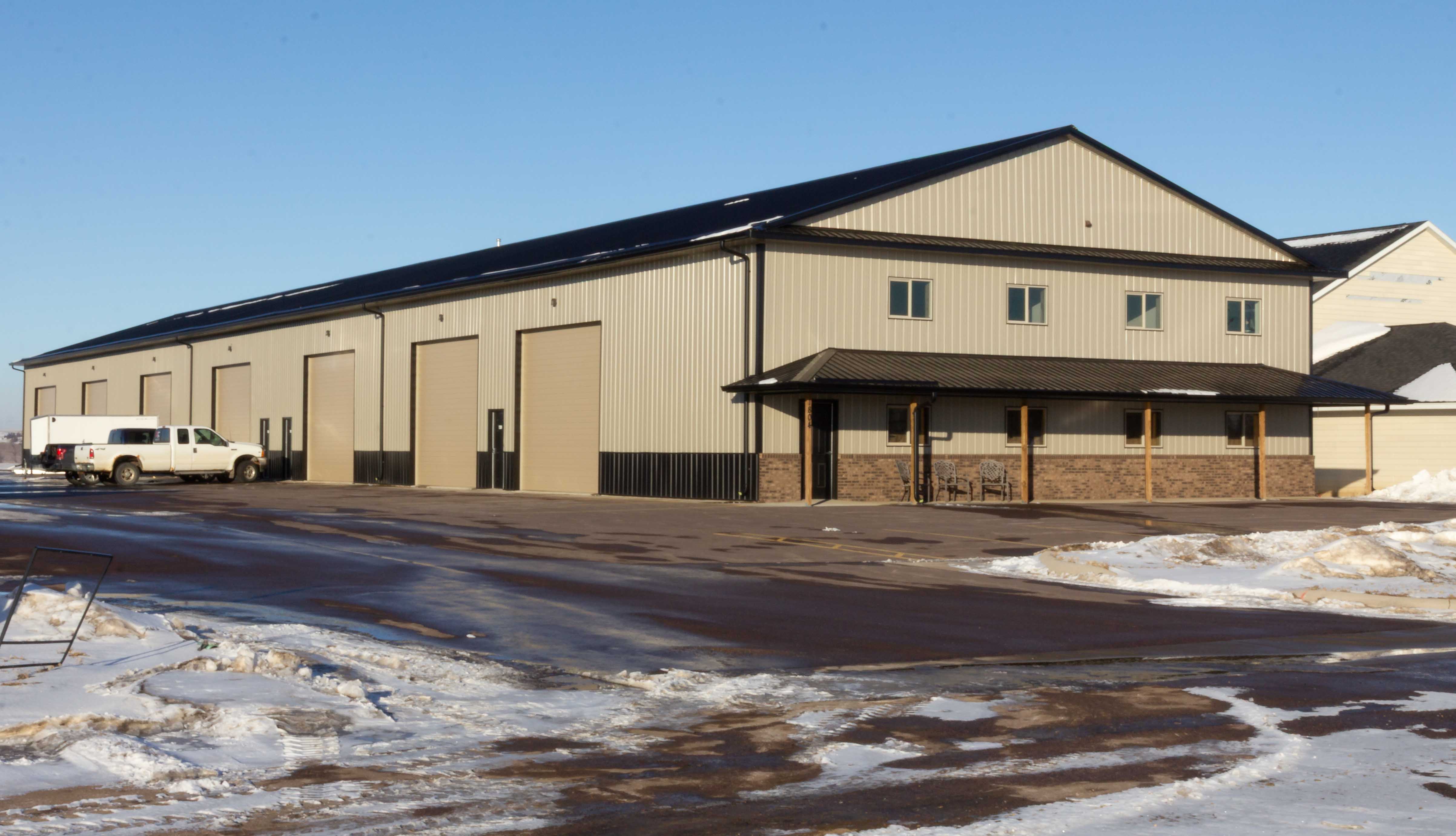 Long tan steel shop building with tall overhead doors and a stone-trimmed covered porch on a clear winter day