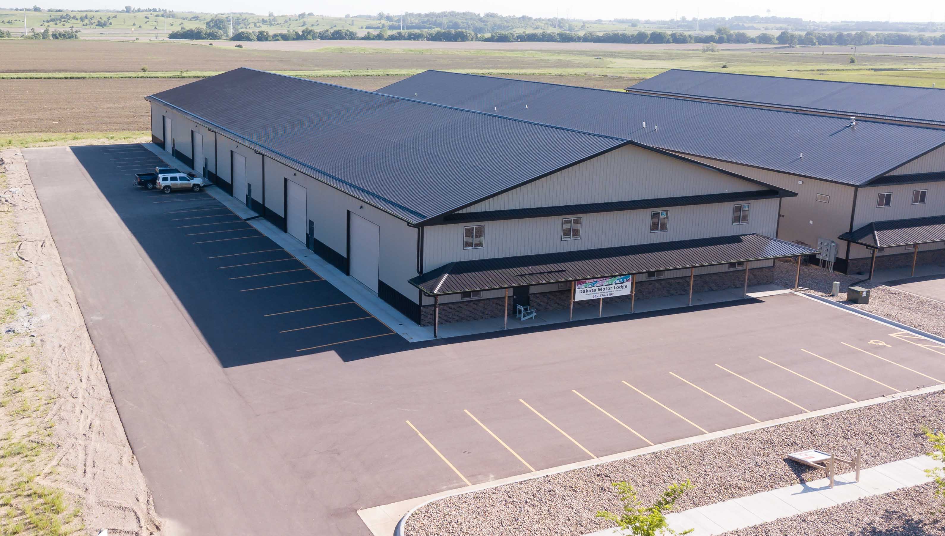 Drone view of beige shop condo buildings with charcoal roofs, a covered entry and a freshly striped asphalt lot