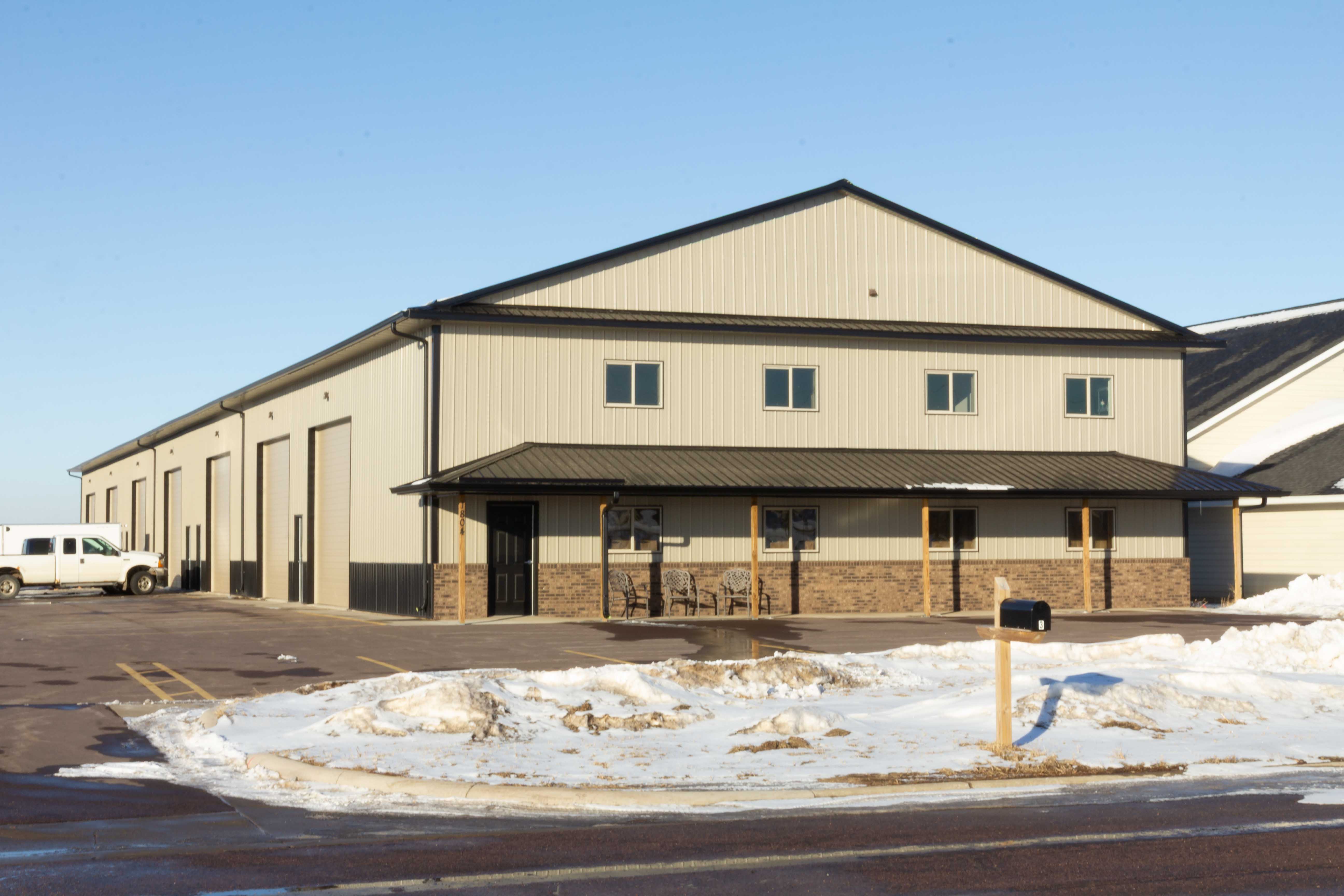 Tan steel shop condo with stone wainscot, timber porch posts and second-floor windows on a snowy day in Brandon, SD